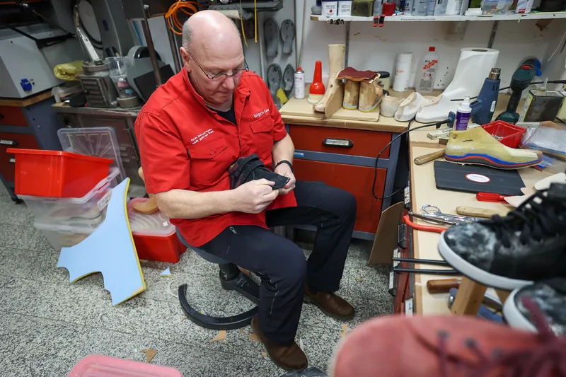 Jürgen Dau arbeitet an der Werkbank an einem Schuh, hinter ihm Holzleisten und Probeschuhe