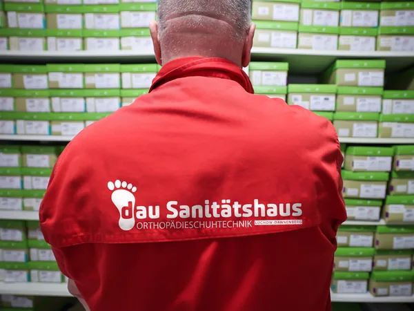 Jürgen Dau von hinten vor dem Schuhlager, auf seiner Jacke das Logo von Dau Sanitätshaus